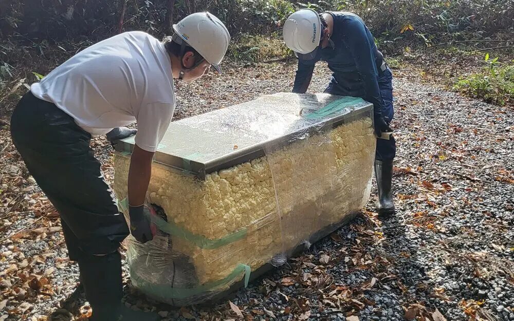 保護フィルムで包まれたバイオトイレ部品を山道で人力搬入するスタッフ