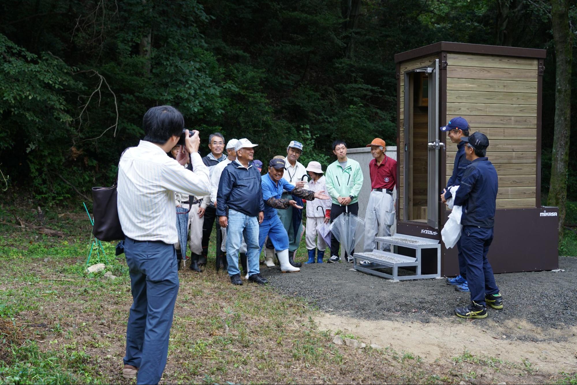 中国新聞社による記念撮影のため新設バイオトイレ前に集まる地域住民と説明スタッフ