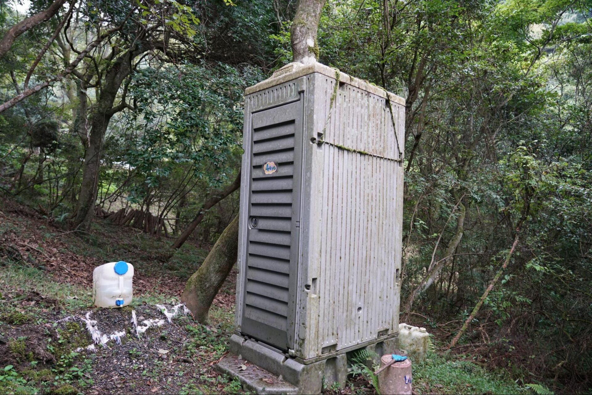 山中に長年設置されていた老朽化した和式簡易トイレと水タンク