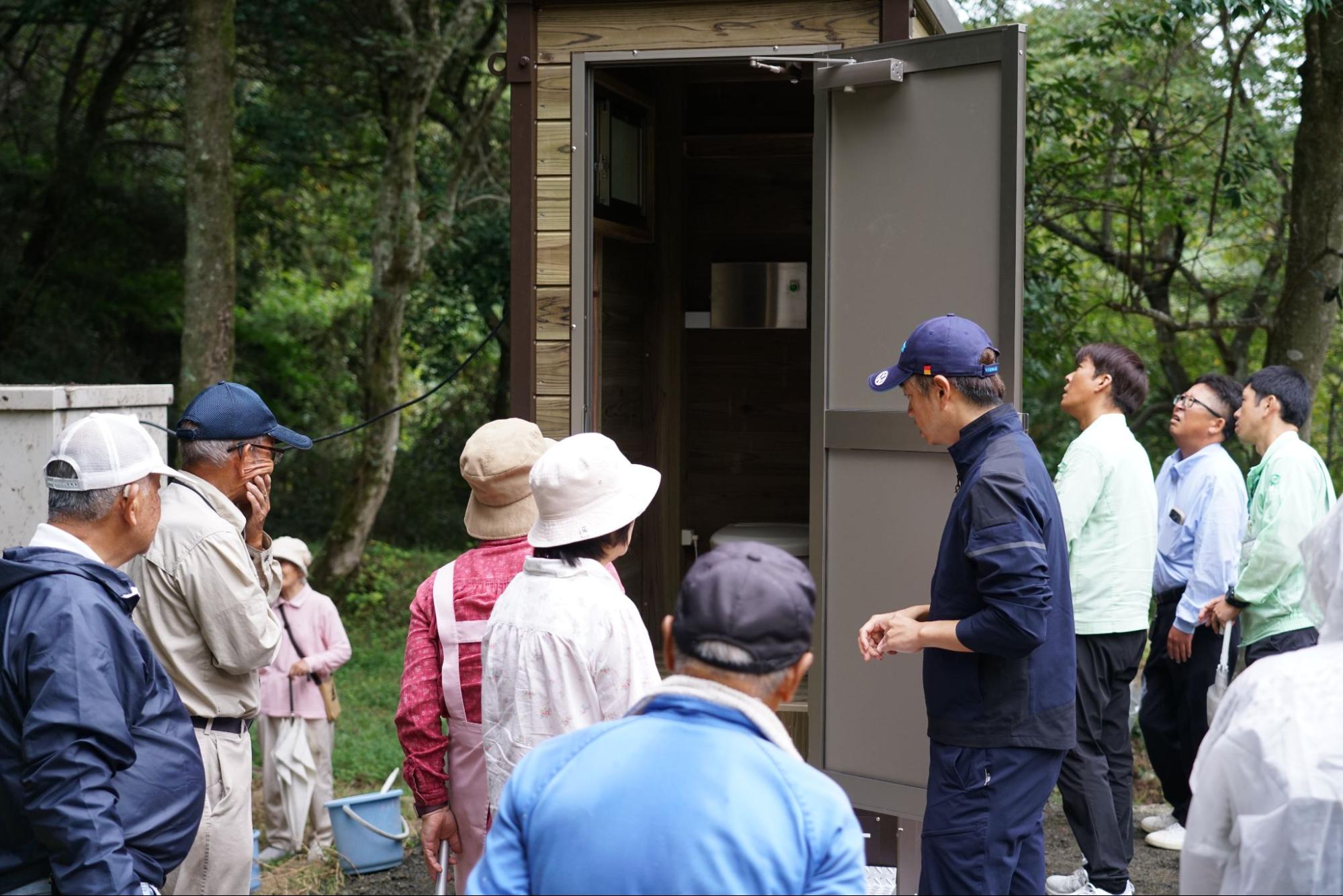 バイオトイレの内部を見学する地域住民たちと、設置状況を説明する関係者の様子